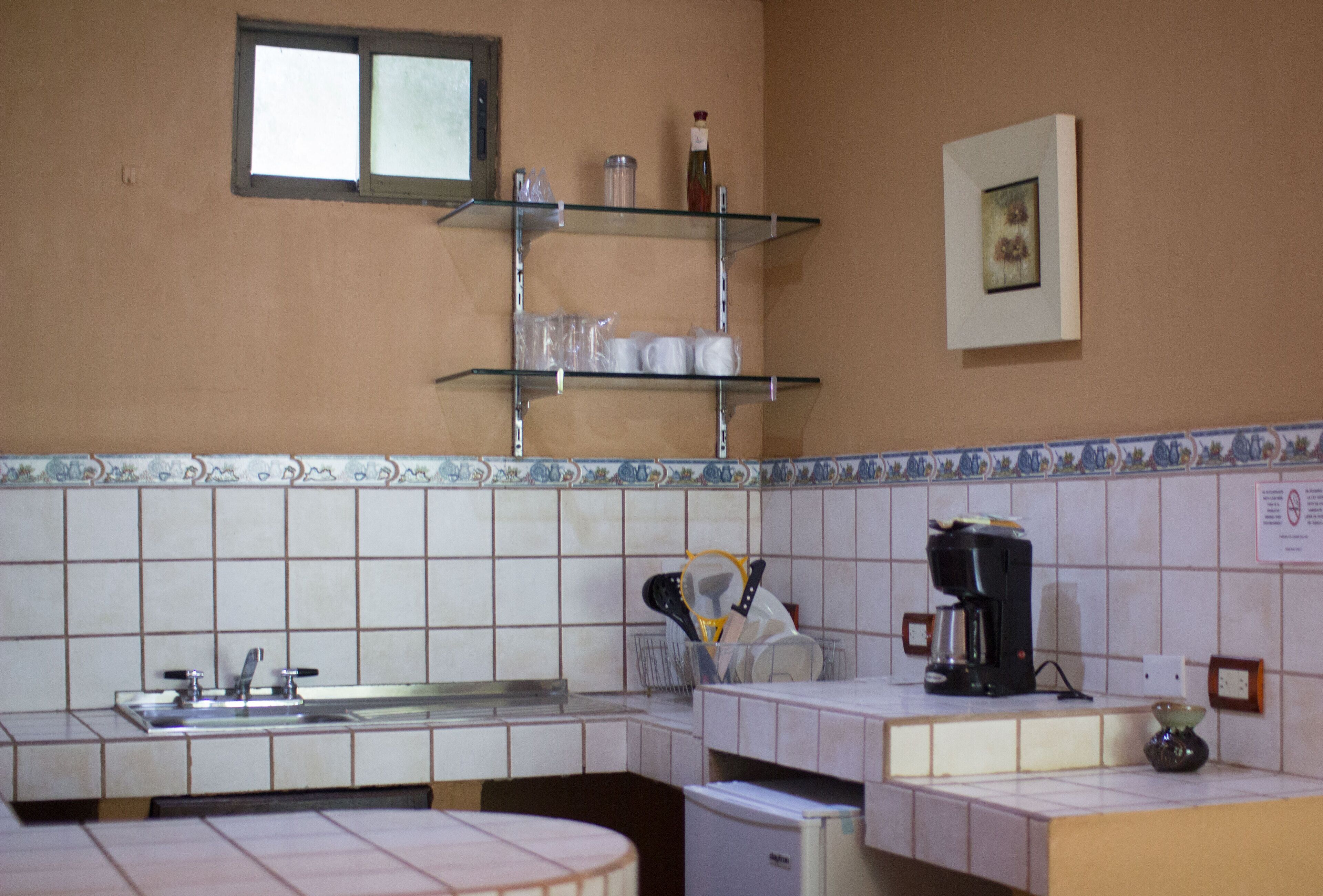 Een keuken met een spoelbak, een koffiezetapparaat en planken met keukengerei.