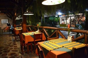 Um restaurante com mesas forradas com toalhas de mesa listradas, cadeiras de madeira e luminárias pendentes.