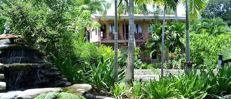 Een tropisch resort met een waterval, weelderige begroeiing en een tweelaags gebouw met balkons.