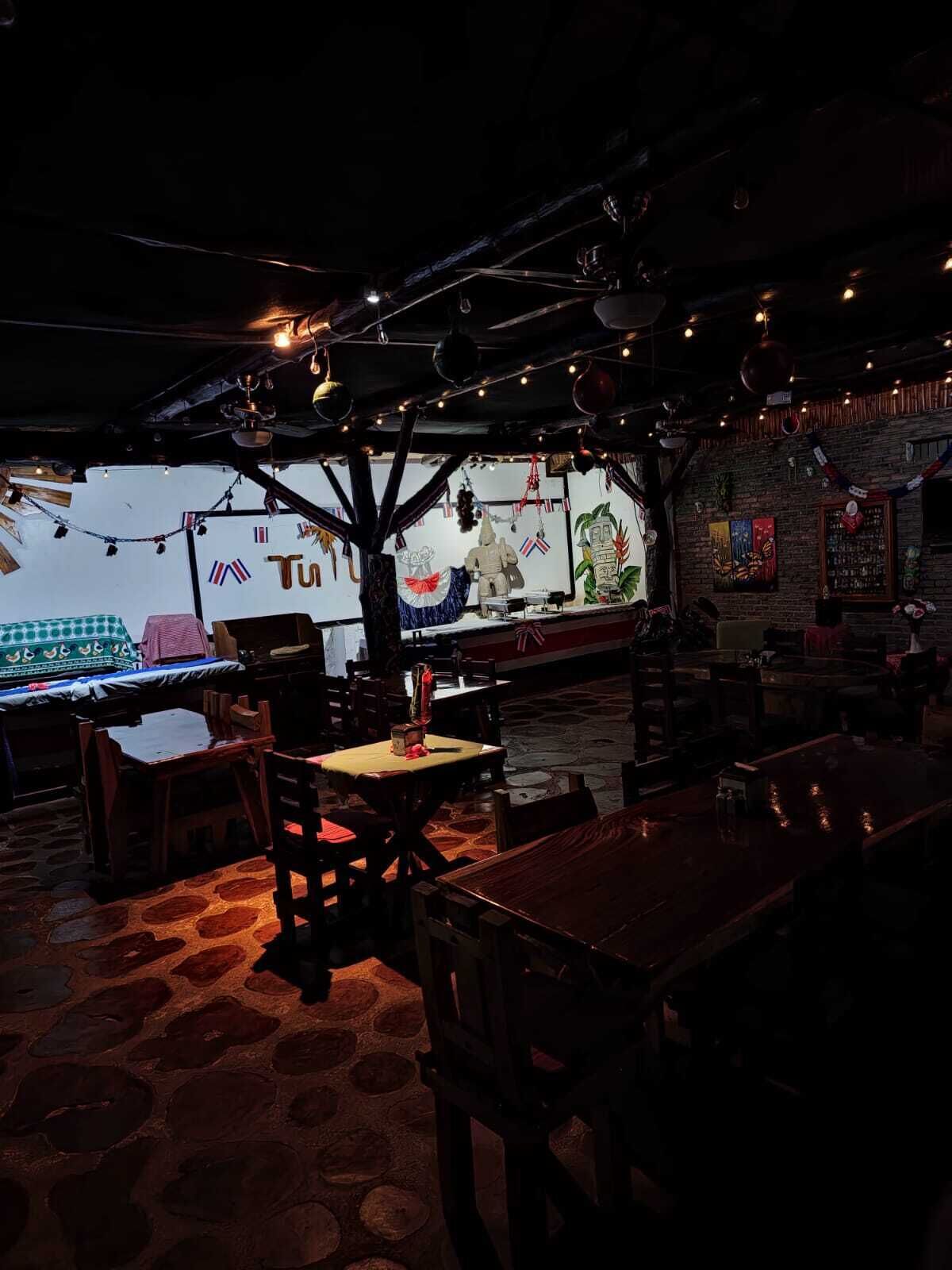An indoor restaurant with wooden tables and chairs, a brick wall with artwork, and string lights on the ceiling.