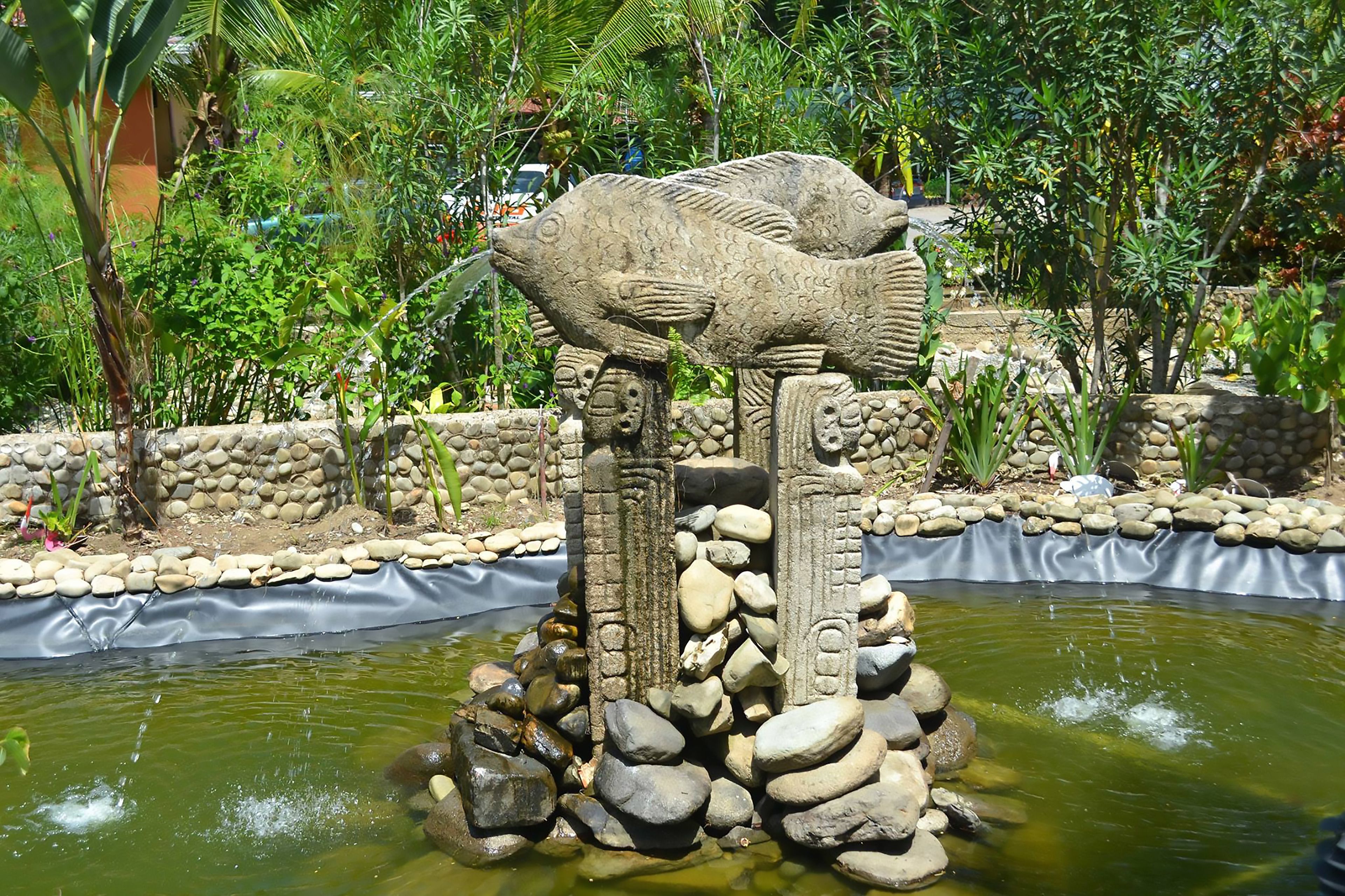 A stone fish sculpture in a garden with a pond.