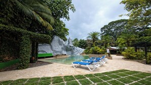A pool area with lounge chairs, a rock formation, and greenery. - Hotel Diuwak (Bahía Ballena)