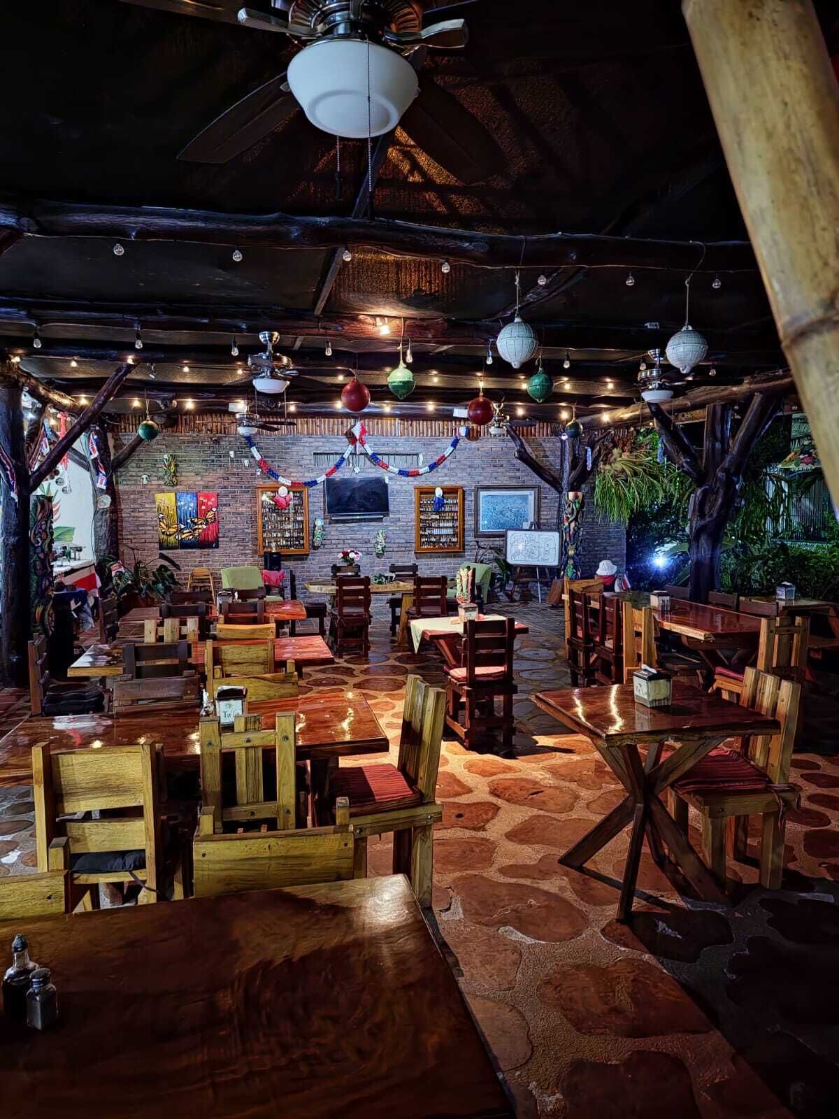Een restaurantruimte met houten tafels en stoelen, een bakstenen muur en hangende lampen.
