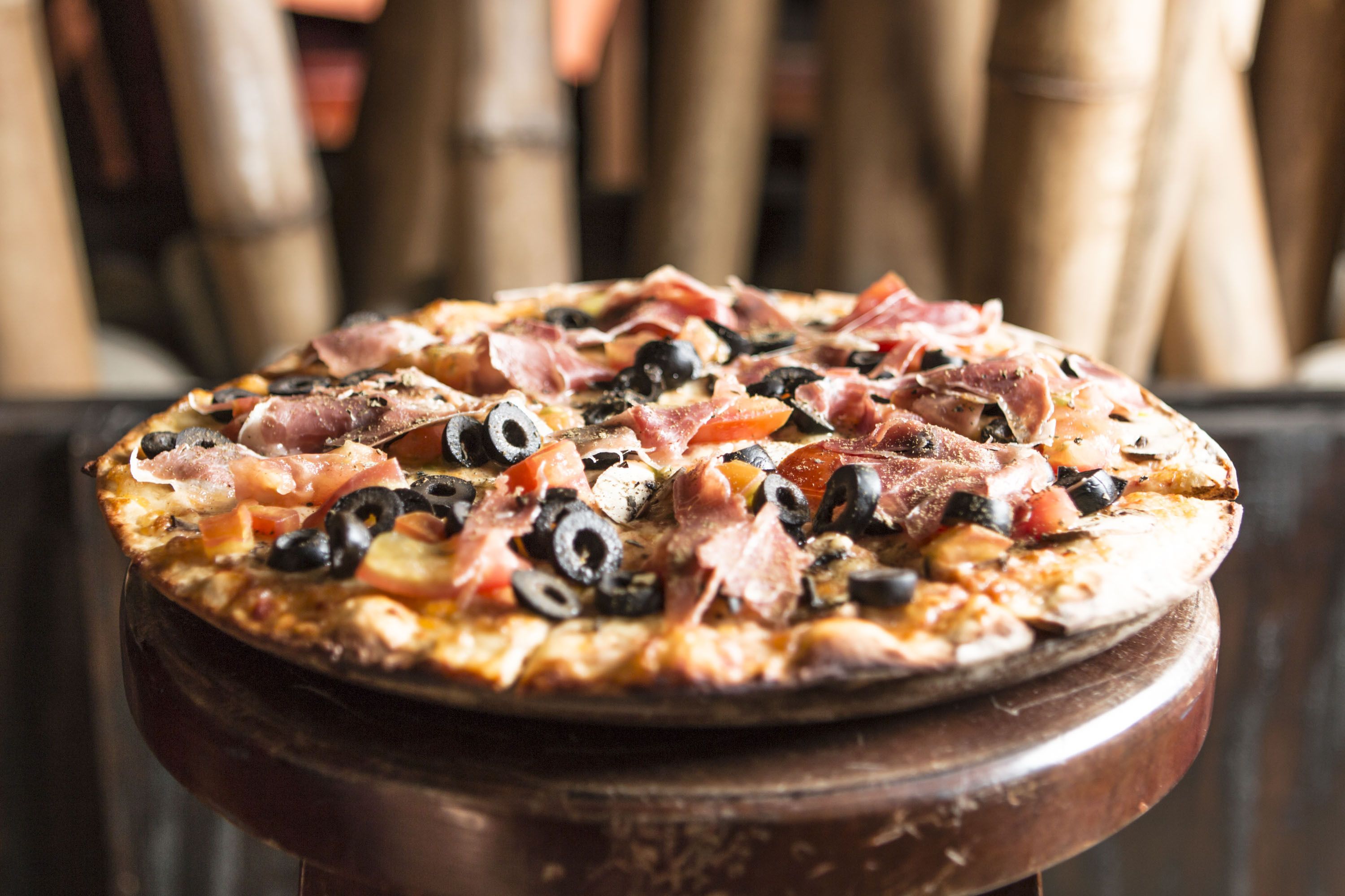 A pizza with various toppings on a wooden stand.