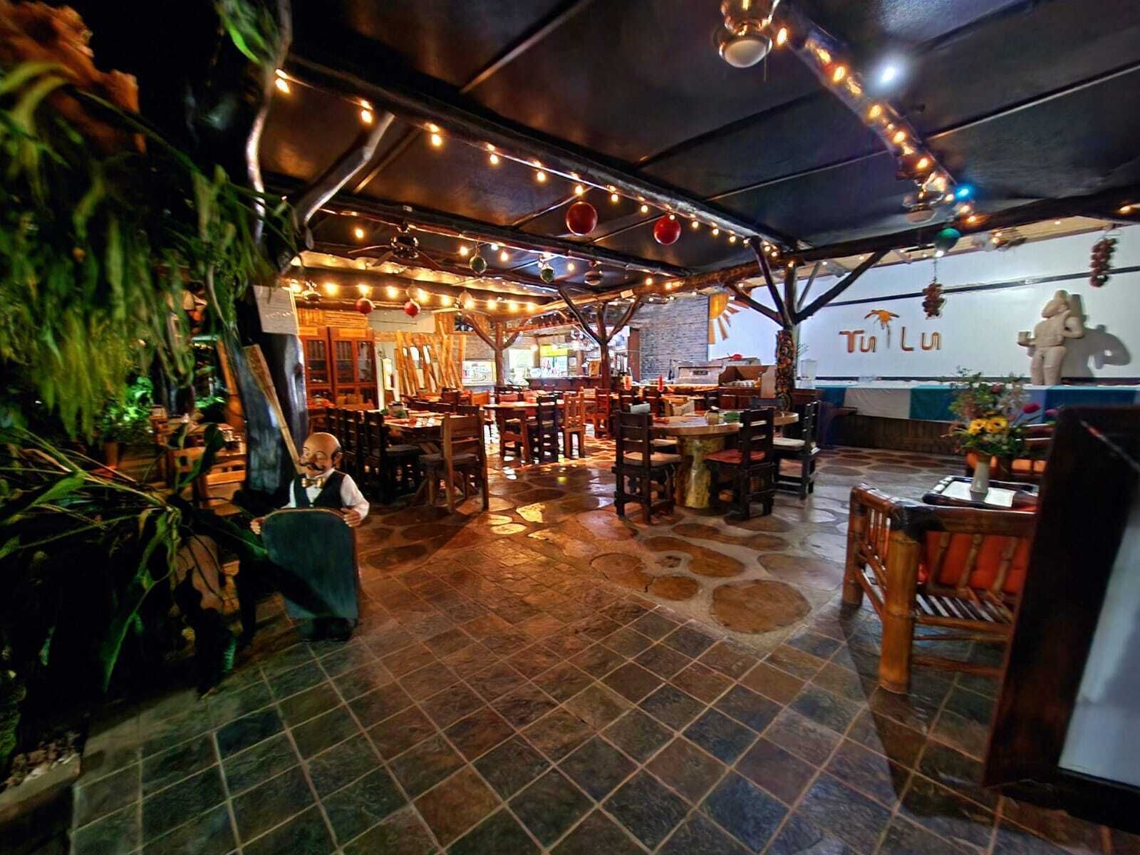 A restaurant with a rustic interior, featuring wooden tables and chairs, a tiled floor, and string lights.