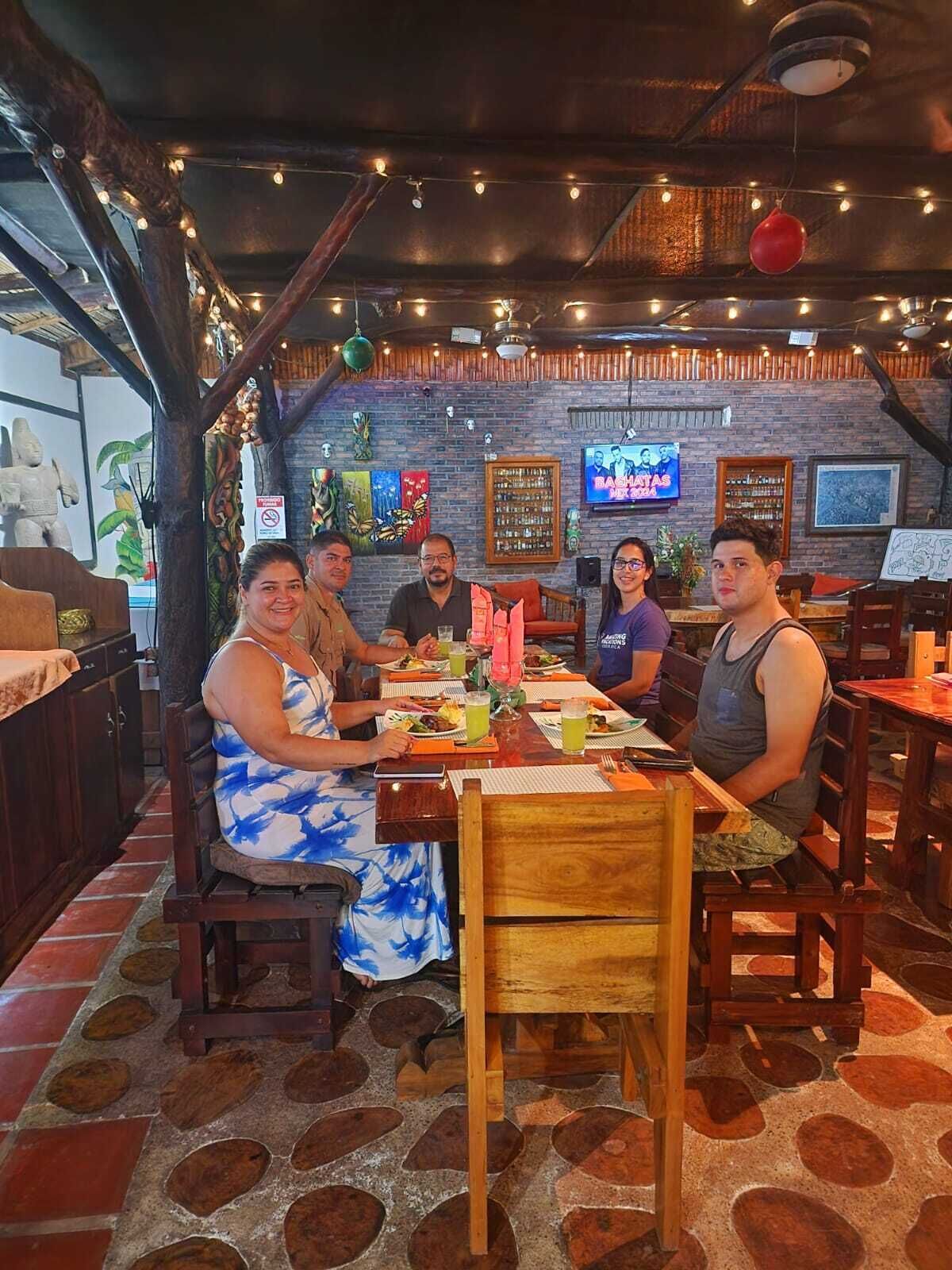 Un grupo de personas cenando en un restaurante con una decoración rústica, paredes de ladrillo y luces colgantes.