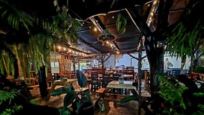 An indoor restaurant with wooden tables and chairs, surrounded by lush green plants. - Hotel Diuwak (Bahía Ballena)