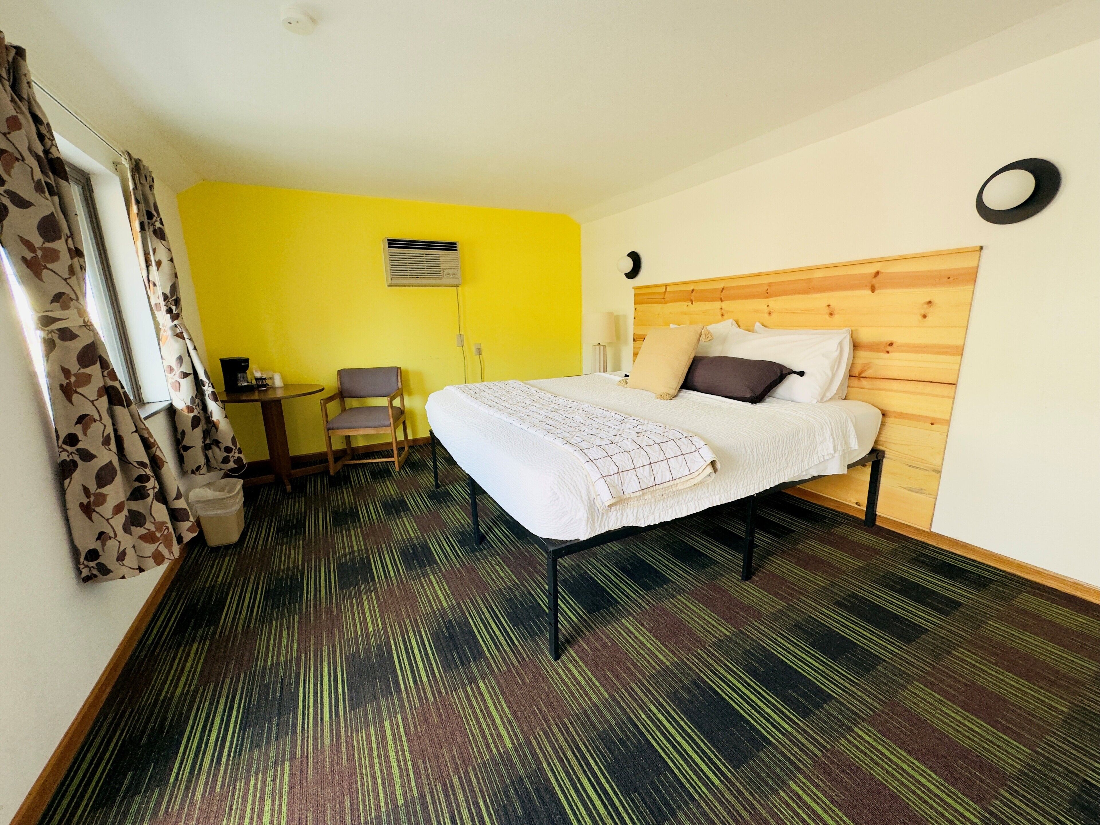 A hotel room with a bed, a chair, a desk, and a small table.