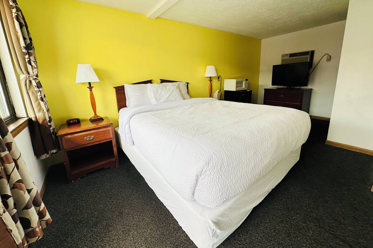 A hotel room with a large bed, two bedside tables with lamps, a TV, and a microwave.