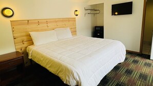 A hotel room with a wooden headboard, a bed with white bedding, a nightstand, a TV mounted on the wall, and a small desk with a chair. - Quality Lodge (Sandusky)