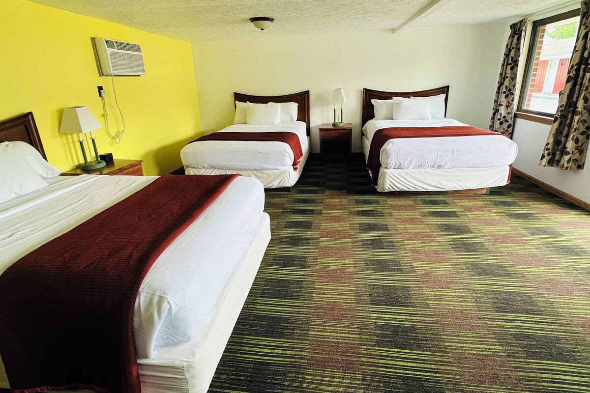 A hotel room with three beds, a patterned carpet, and a yellow wall.