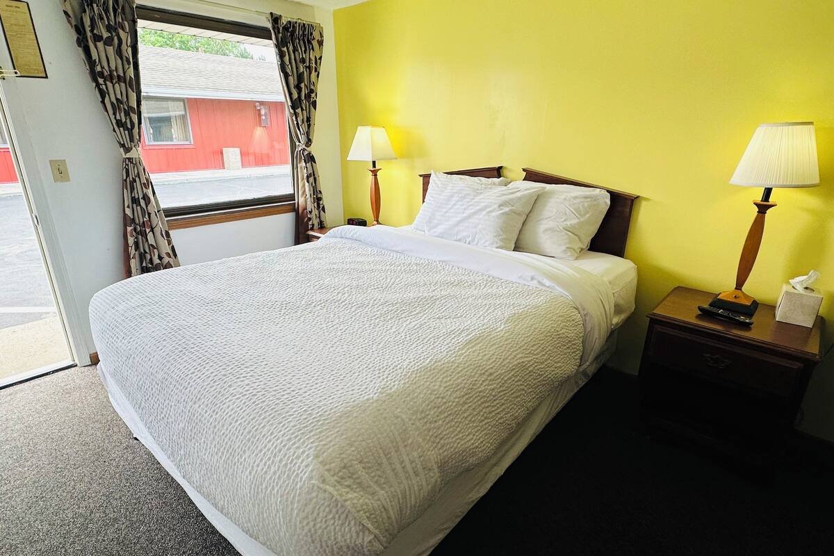 A hotel room with a bed, two bedside lamps, a nightstand, and a window with curtains.