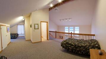 A bedroom with a bunk bed, carpeted floor, wooden ceiling beams, and a staircase leading to an upper level.
