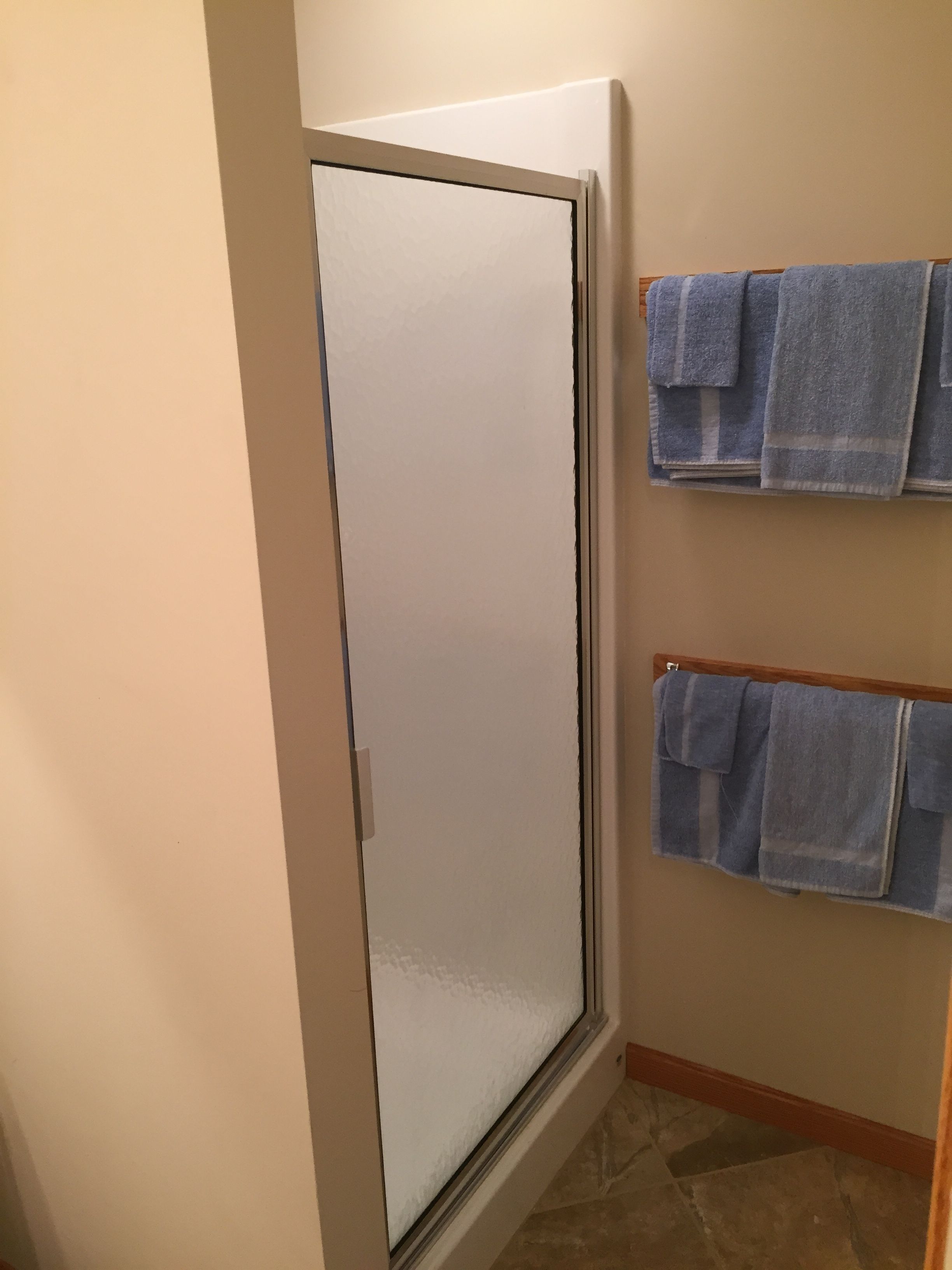A bathroom with a glass shower door, a towel rack with two towels, and a tiled floor.