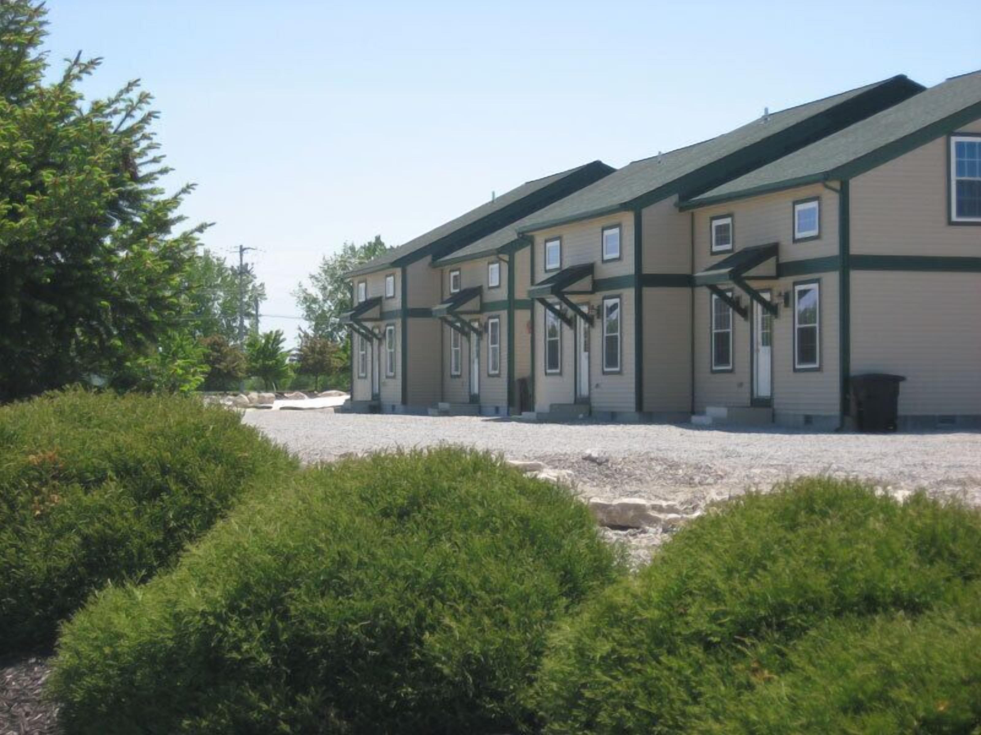 A row of two-story buildings with a gravel driveway and green landscaping.