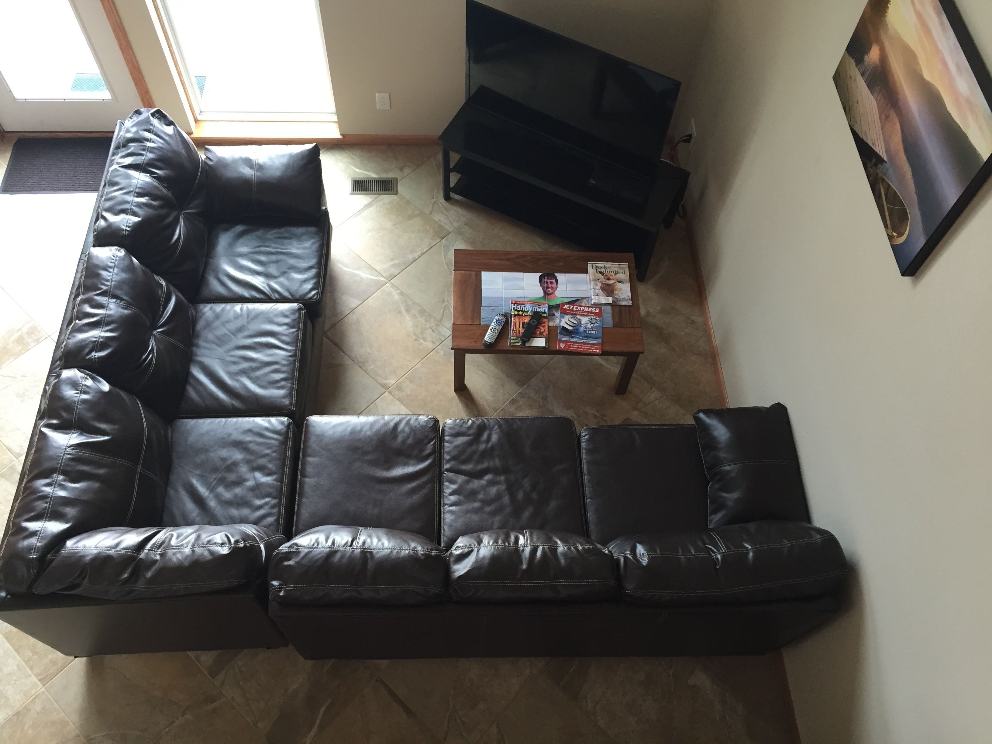 A living room with a black leather sectional sofa, a wooden coffee table with magazines, and a black TV stand.