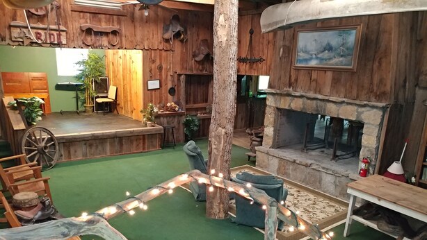 A rustic interior with a wooden stage, seating area, and a stone fireplace. - Arrowmont Stables & Cabins (Cullowhee)