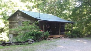 A rustic log cabin with a porch, surrounded by greenery and a gravel driveway. - Arrowmont Stables & Cabins (Cullowhee)