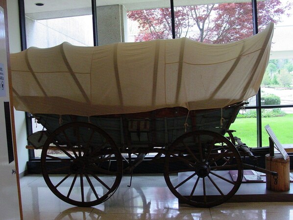 A covered carriage displayed indoors with large windows in the background. - Arrowmont Stables & Cabins (Cullowhee)