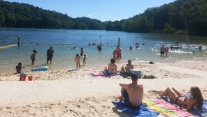 A beach with people swimming and playing in the water, a sandy shore with beachgoers, and a forested hillside in the background. - Arrowmont Stables & Cabins (Cullowhee)
