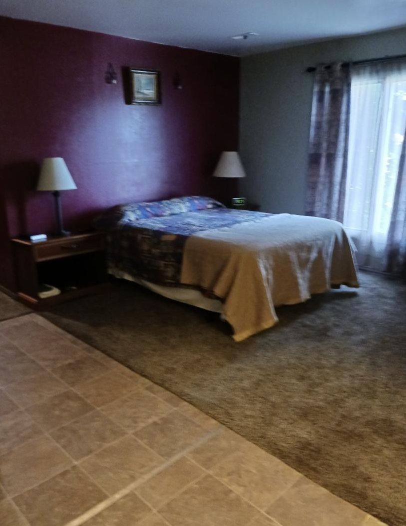 A hotel room with a bed, two bedside lamps, a nightstand, and a window with curtains.