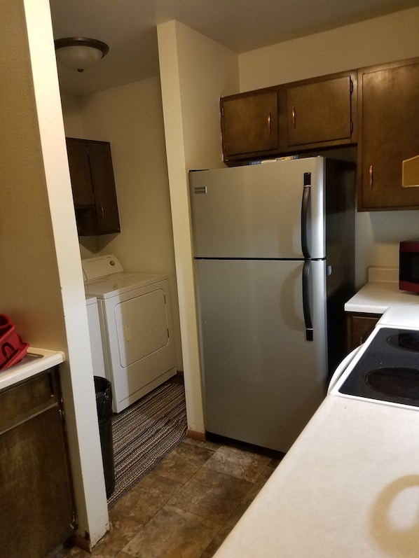 A compact kitchen with a stainless steel refrigerator, a washing machine, and wooden cabinets. - Dakota Rose Inn (Underwood)