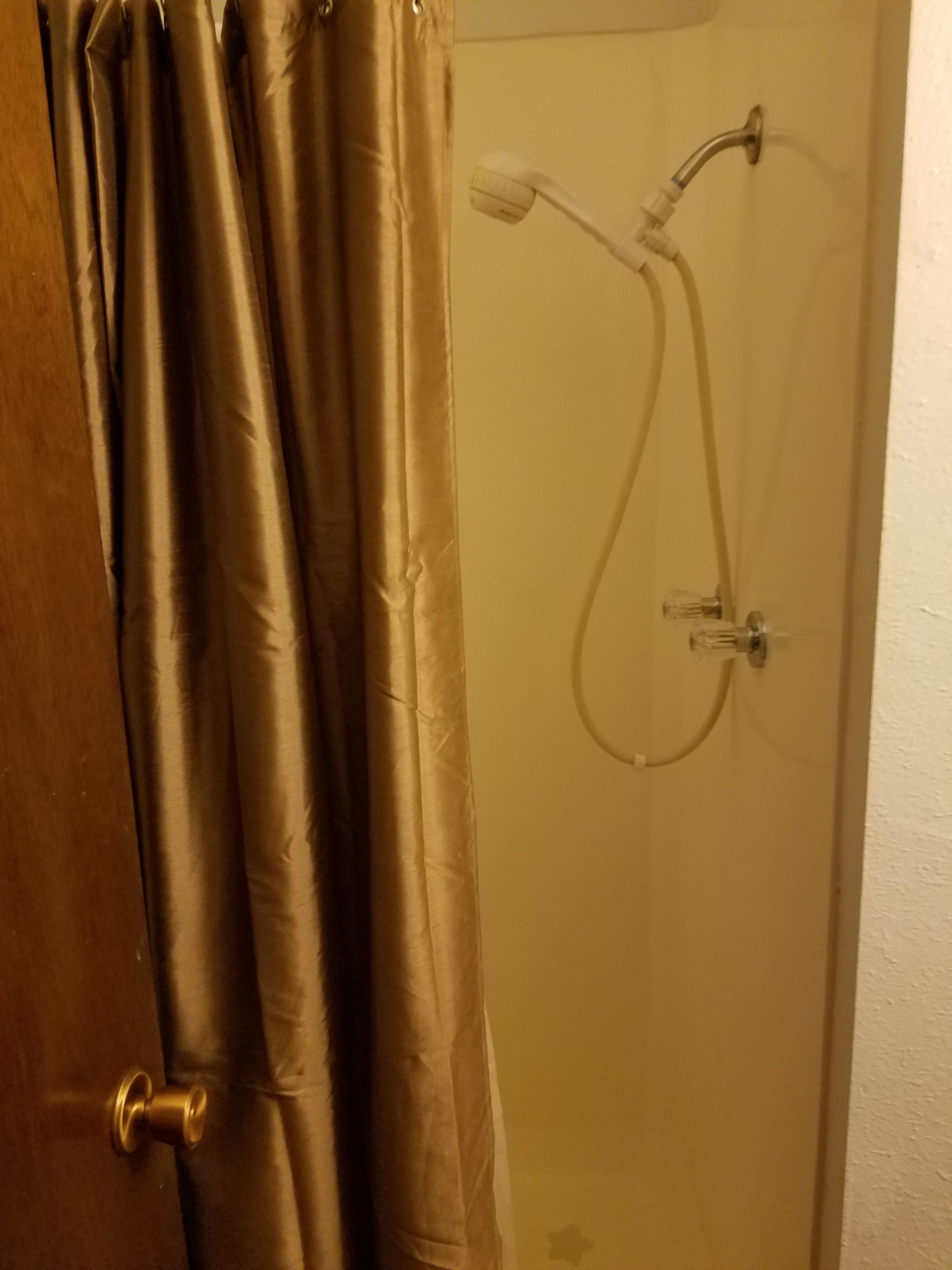 A bathroom with a shower, a door with a golden handle, and a curtain.