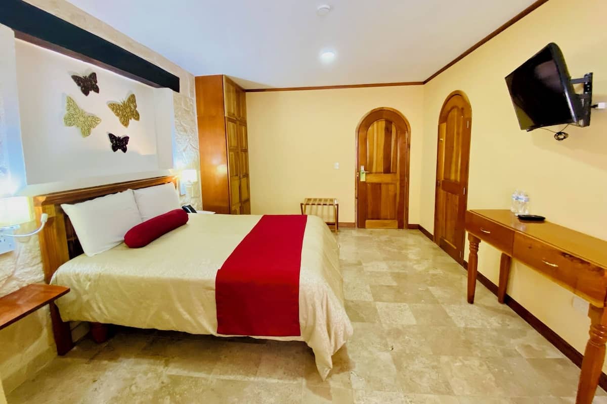 A hotel room with a bed, a desk, a television, and a door.