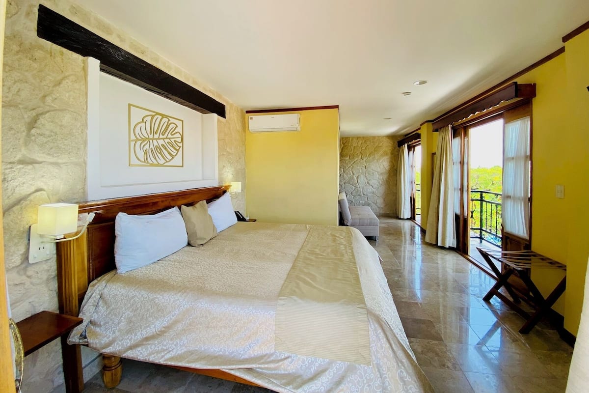 A spacious bedroom with a large bed, a bedside table, a wall-mounted lamp, and a view of the balcony.