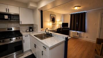 A compact kitchen with a stove, sink, and cabinets, a small dining area with a table and chairs, and a TV in the background.