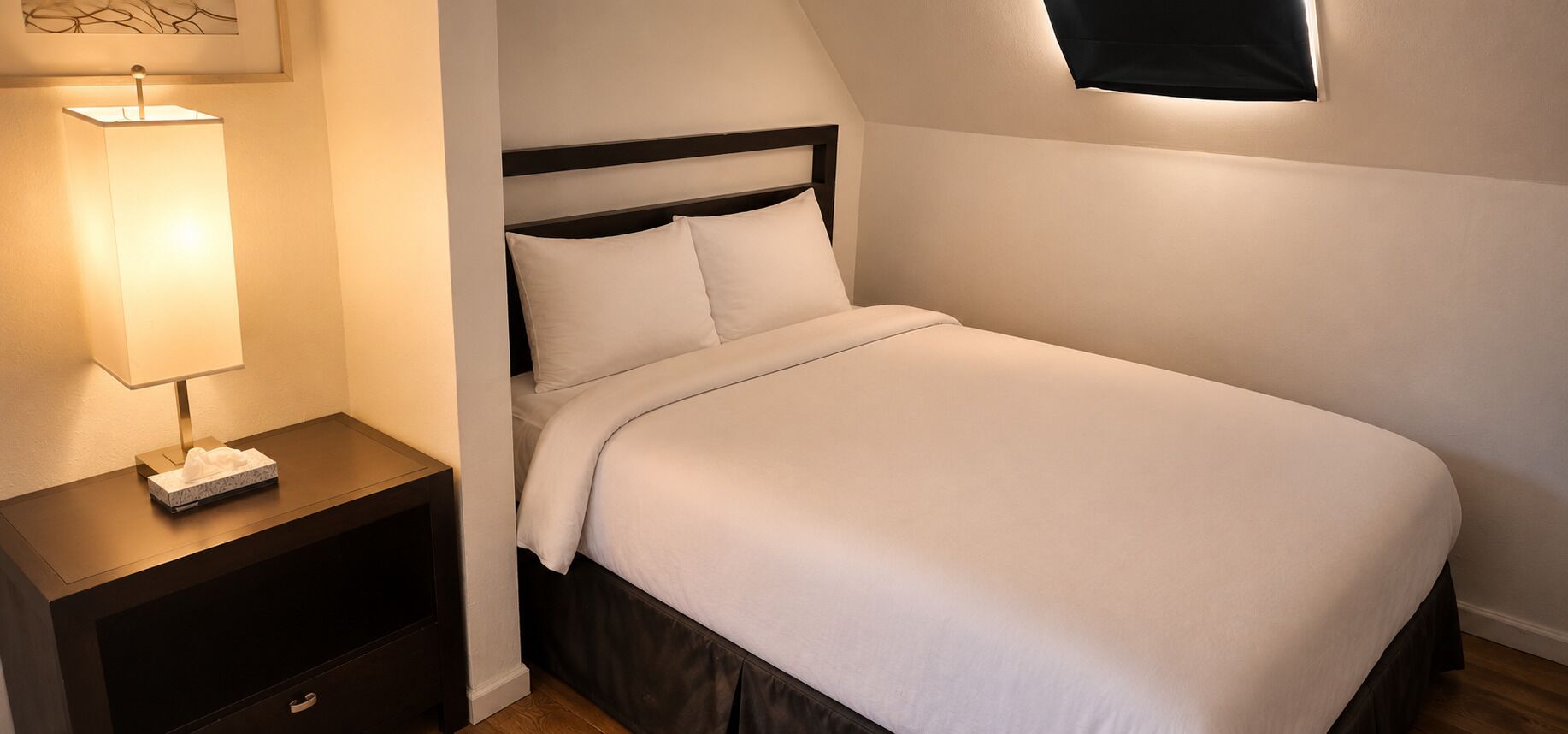 A neatly made bed with a headboard, a bedside lamp, and a nightstand with a tissue box.