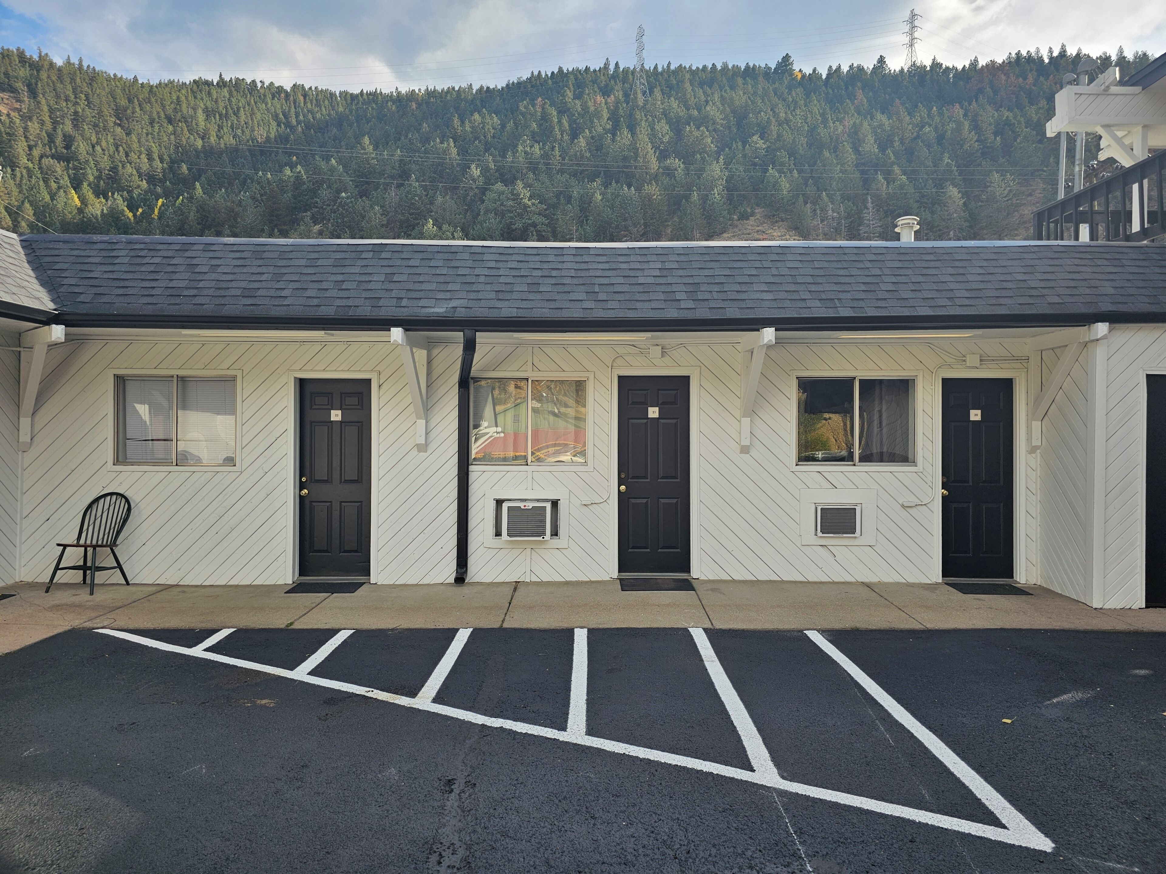 A building with a parking lot in front, a black chair outside, and a forested hill in the background.
