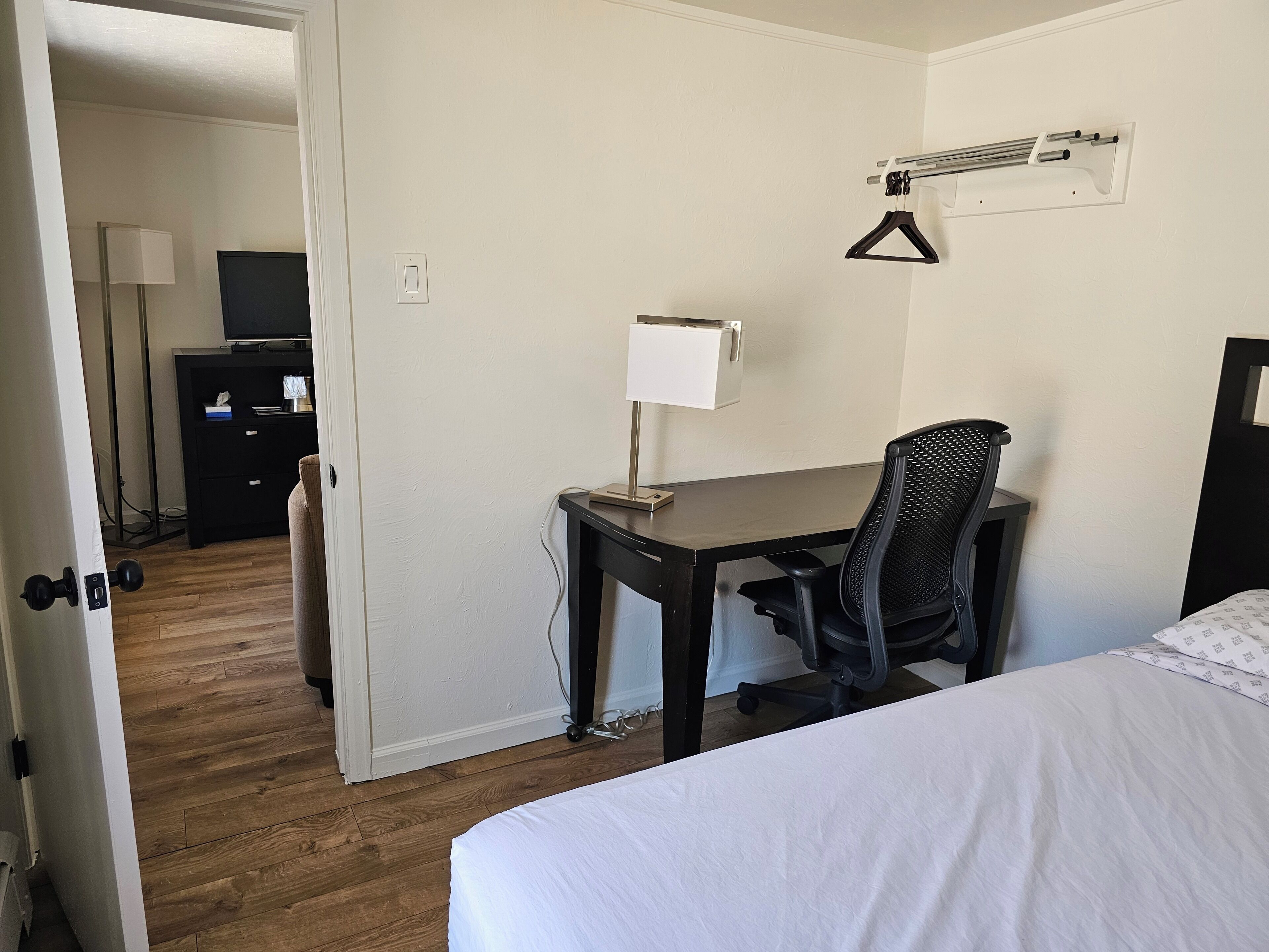 Habitación de hotel con cama, escritorio con silla, lámpara, televisor sobre una cómoda y aire acondicionado de pared.