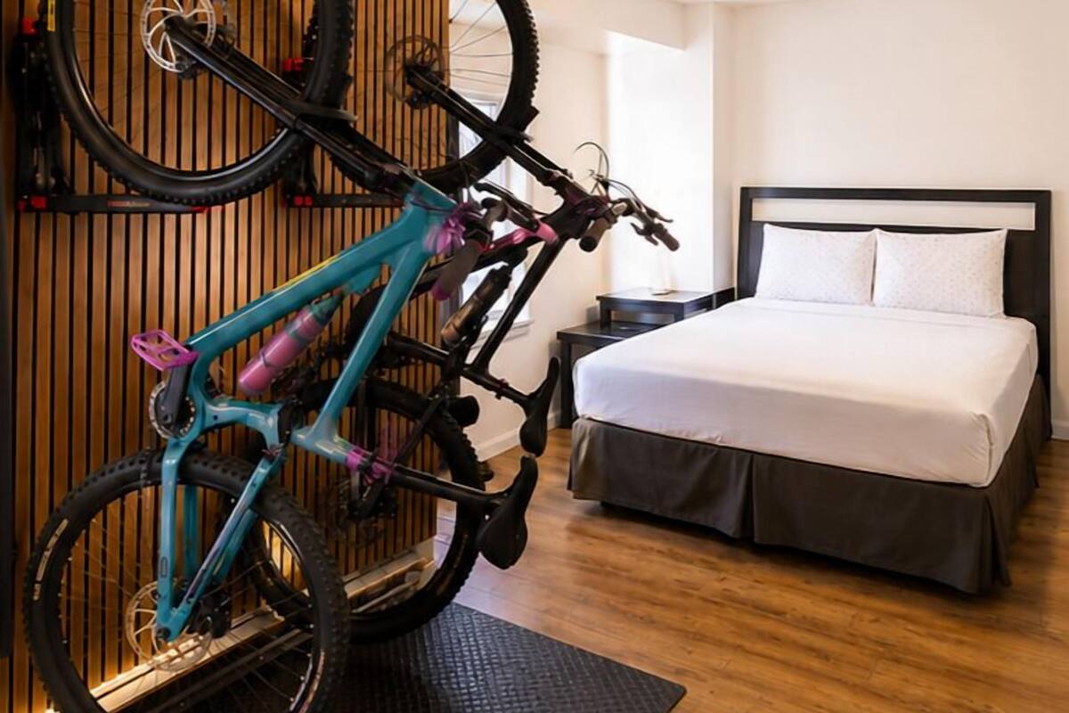 A room with a bed, a nightstand, a wall-mounted bike rack, and a wooden slat wall.
