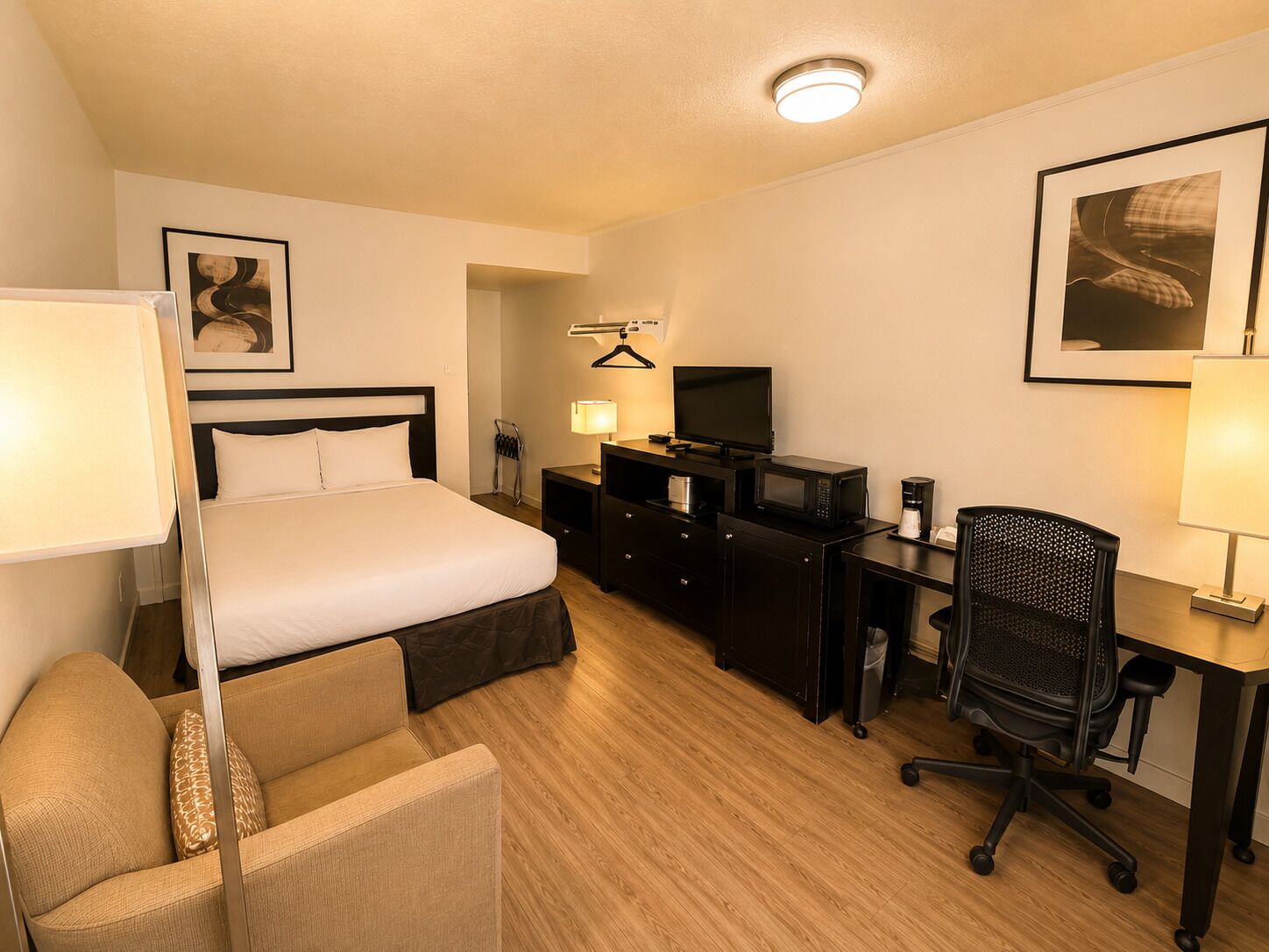 Una habitación de hotel con cama, escritorio, silla, televisor y lámpara.