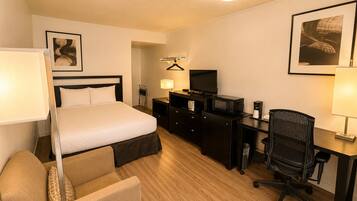 Una habitación de hotel con cama, escritorio, silla, televisor y lámpara.
