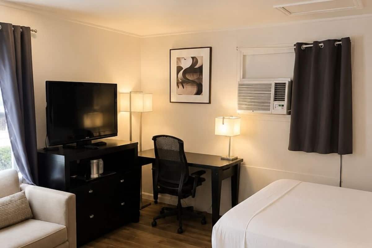 A hotel room with two beds, a desk with a chair, a television, a desk lamp, and a picture on the wall.