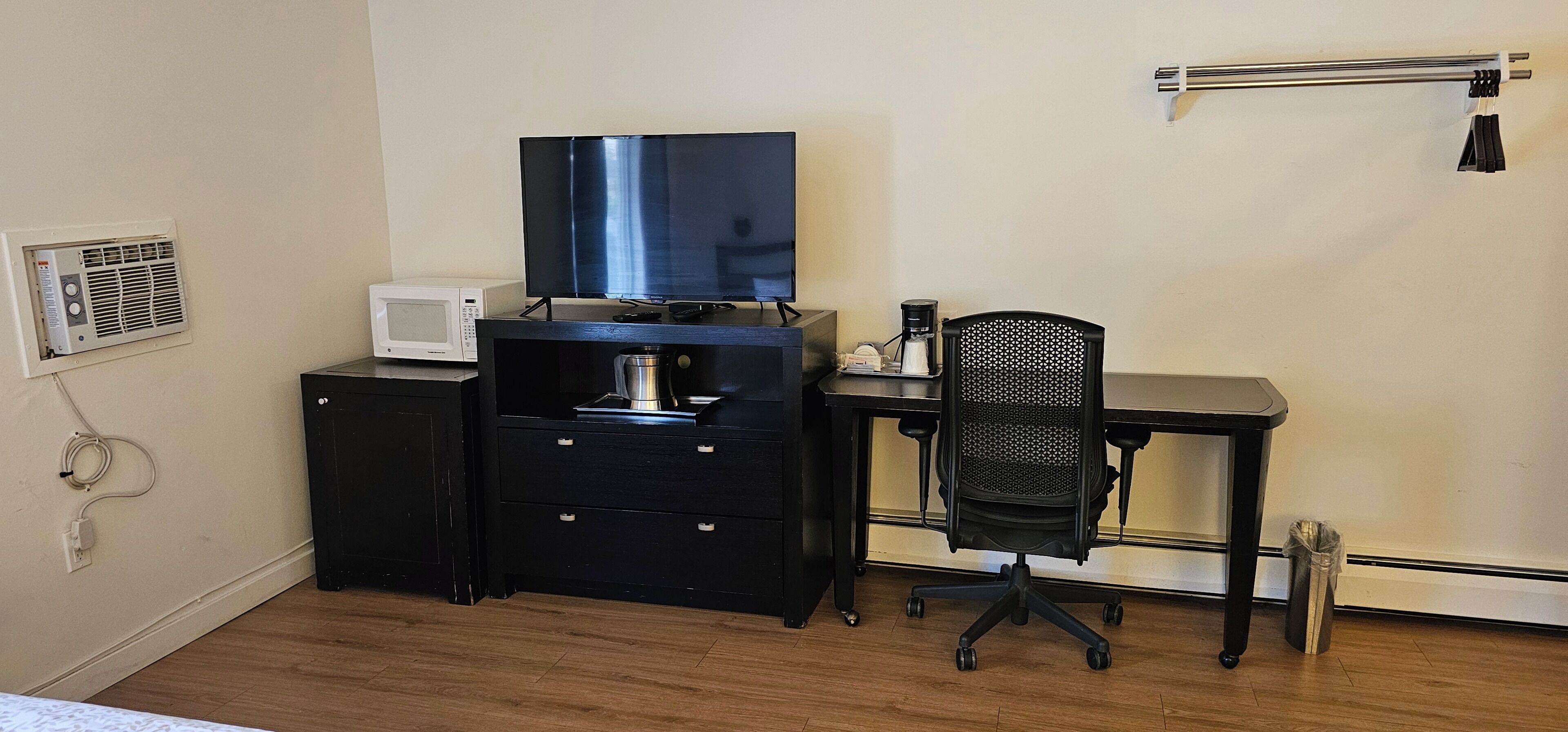 Une chambre équipée d’un bureau, d’une chaise, d’une télévision, d’un four à micro-ondes et d’une machine à café.
