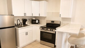A compact kitchen with white cabinets, a stainless steel refrigerator, a coffee maker, a microwave, and a stove. - H & H Motor Lodge (Idaho Springs)