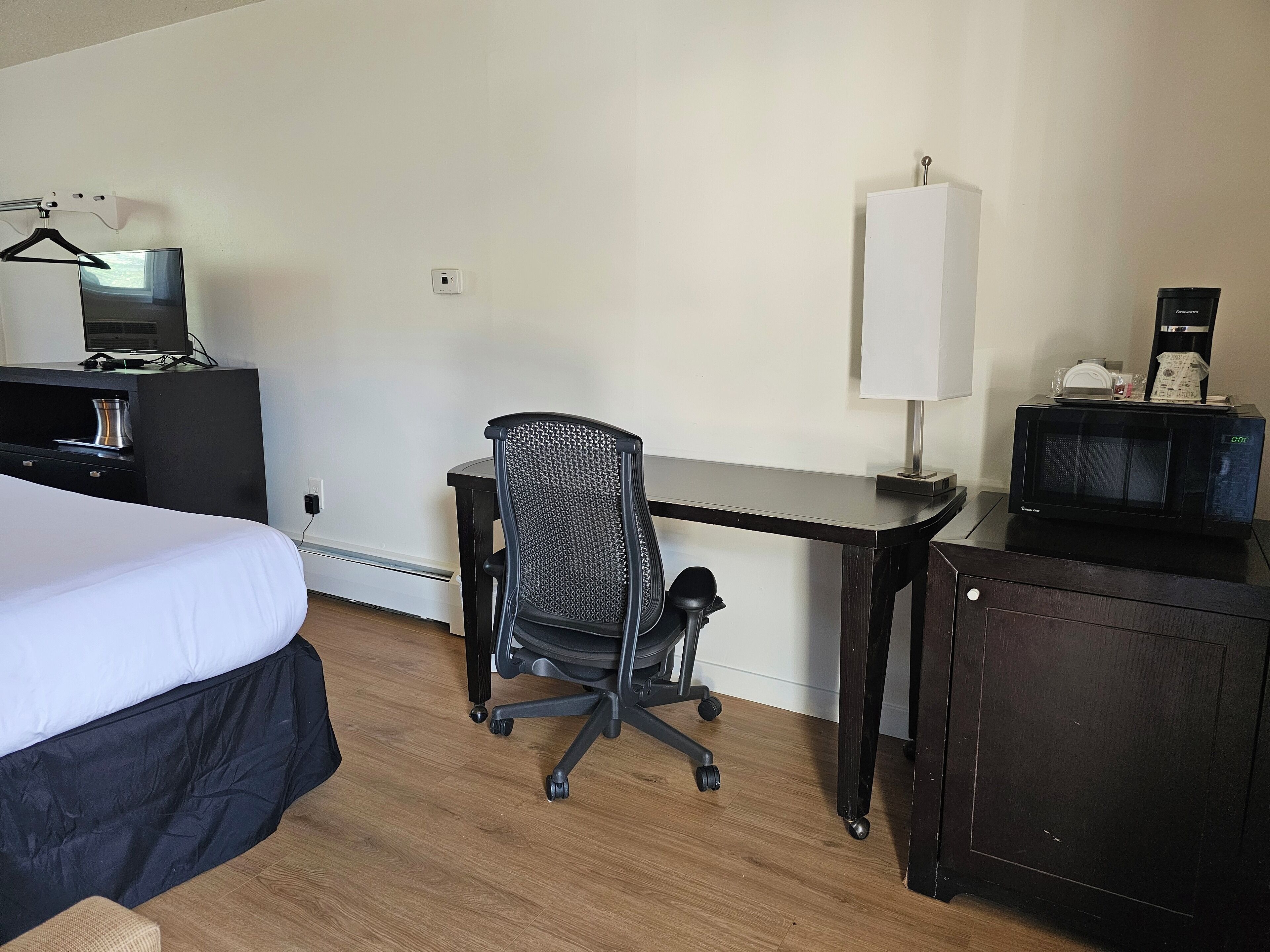 A hotel room with a bed, a desk, a chair, a microwave, and a coffee maker.