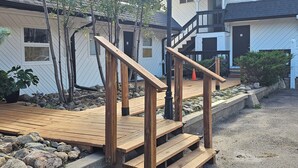 A wooden deck leading to a house with a stone pathway, surrounded by rocks and plants.