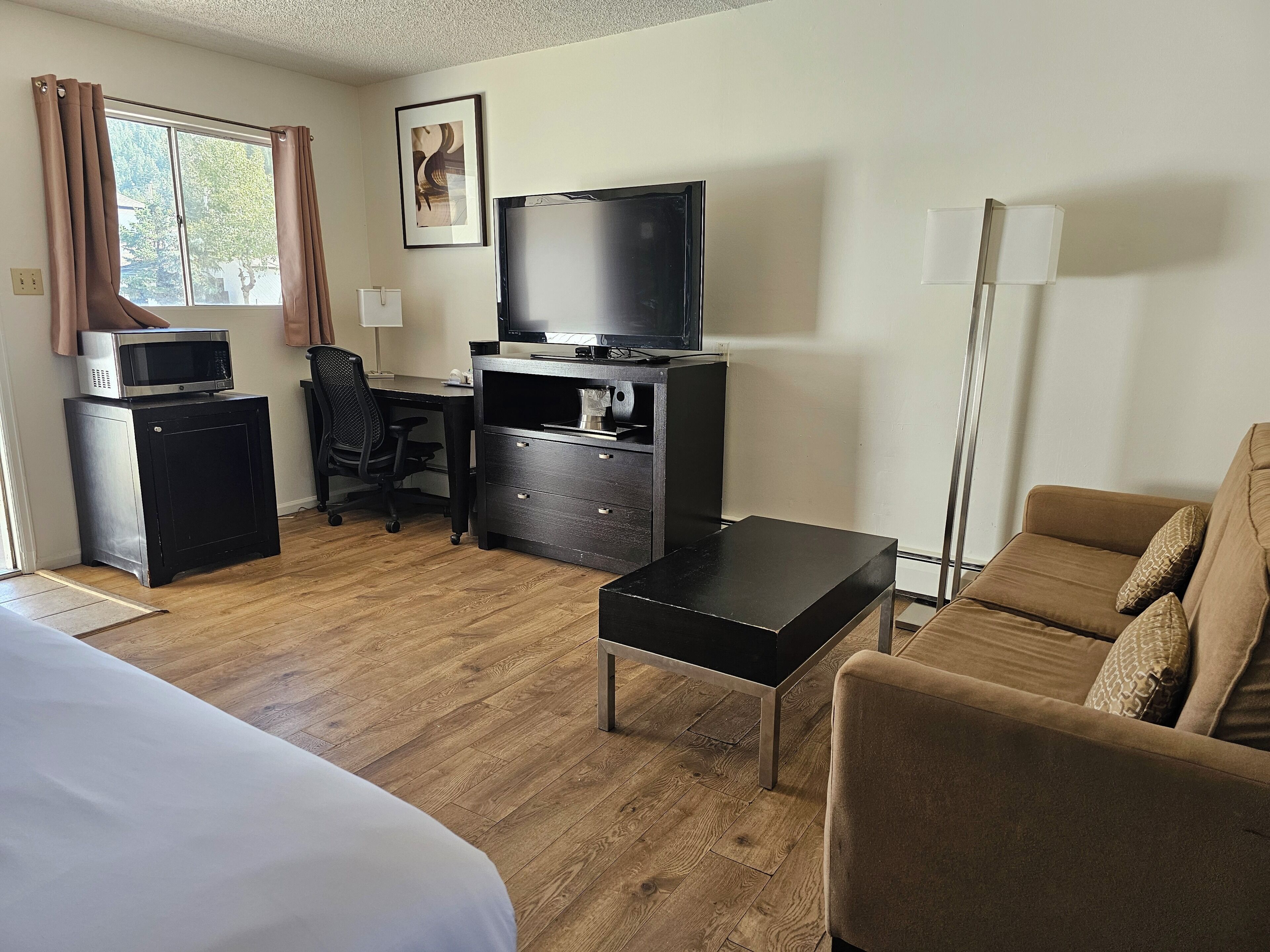 Habitació d'hotel amb un llit, un escriptori amb un ordinador i una televisió, un sofà i una làmpada.