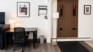 A hotel room with a desk, chair, TV, framed artwork, and a wooden door with a handle.