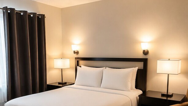 A hotel room with a large bed, two bedside tables with lamps, a chair, and a curtain.