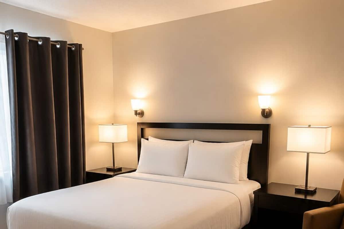 A hotel room with a large bed, two bedside tables with lamps, a chair, and a curtain.