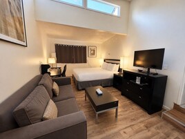 Habitación de hotel con cama, sofá, televisor y escritorio.