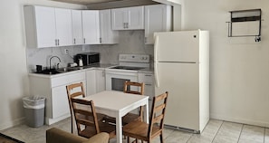 A compact kitchen with white cabinets, a white refrigerator, a stove, a microwave, and a dining table with chairs. - H & H Motor Lodge (Idaho Springs)