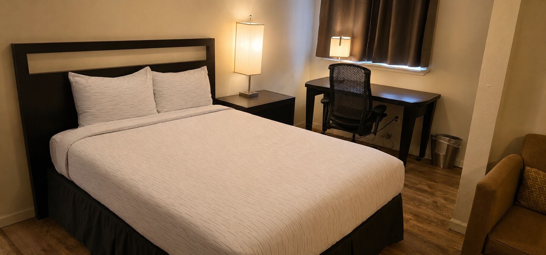 A hotel room with a large bed, bedside tables, a desk, a chair, and a window with curtains.