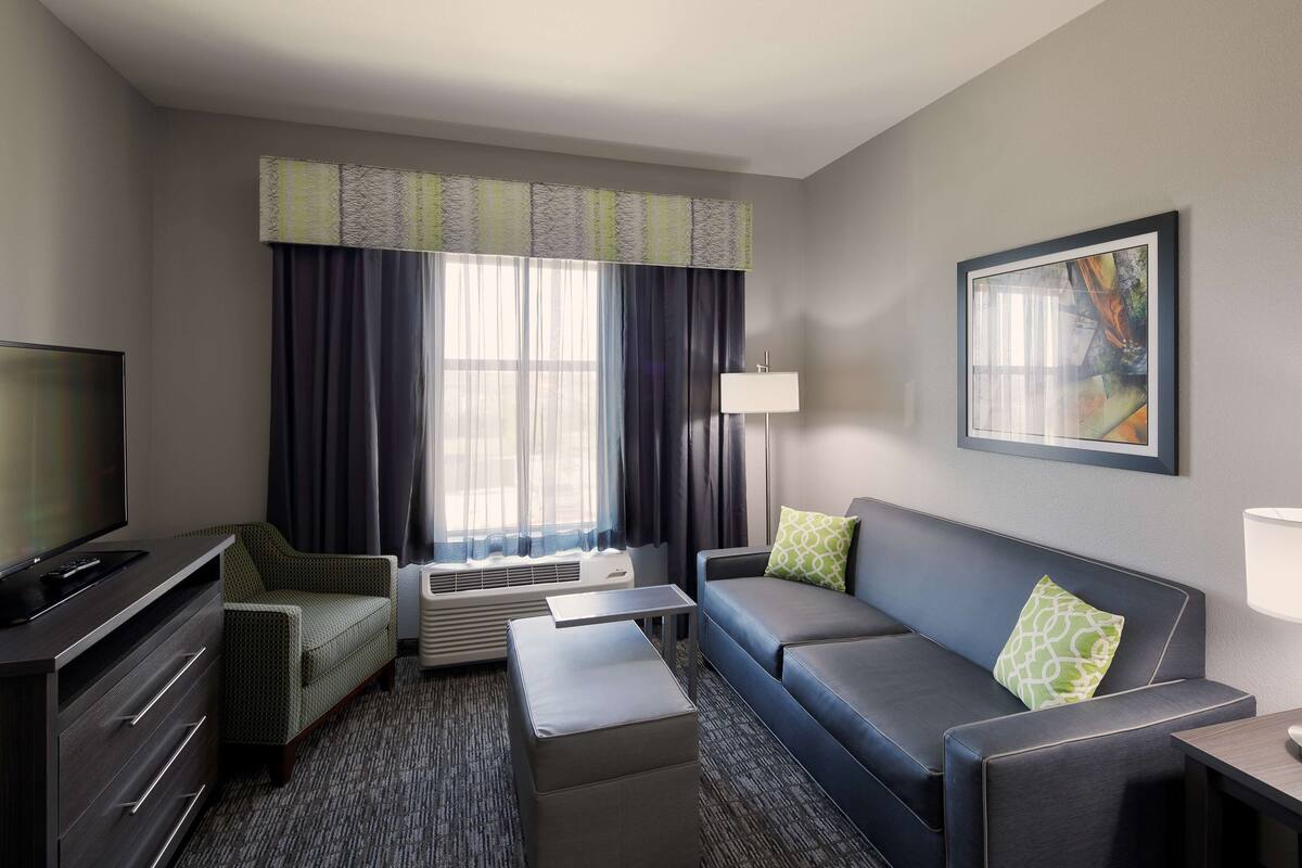 A hotel room with a sofa, a TV, a desk, a lamp, and a painting on the wall.