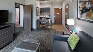 Une chambre d’hôtel équipée d’une télévision, d’un canapé, d’une petite table, d’un coin cuisine et d’une salle de bain.